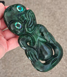 Green jade carving held in a hand against a neutral background