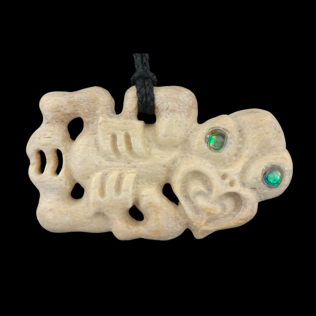 Carved bone pendant with green eyes on a black background