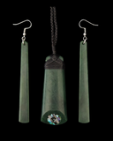 Greenstone jewelry set featuring a central pendant and two matching drop earrings on a solid black background. The central pendant is a tapered greenstone piece with a dark braided cord wrap and a small iridescent shell inlay near the bottom.