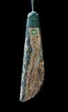 Carved wooden pendant with intricate patterns and a central eye-like gemstone on a black background