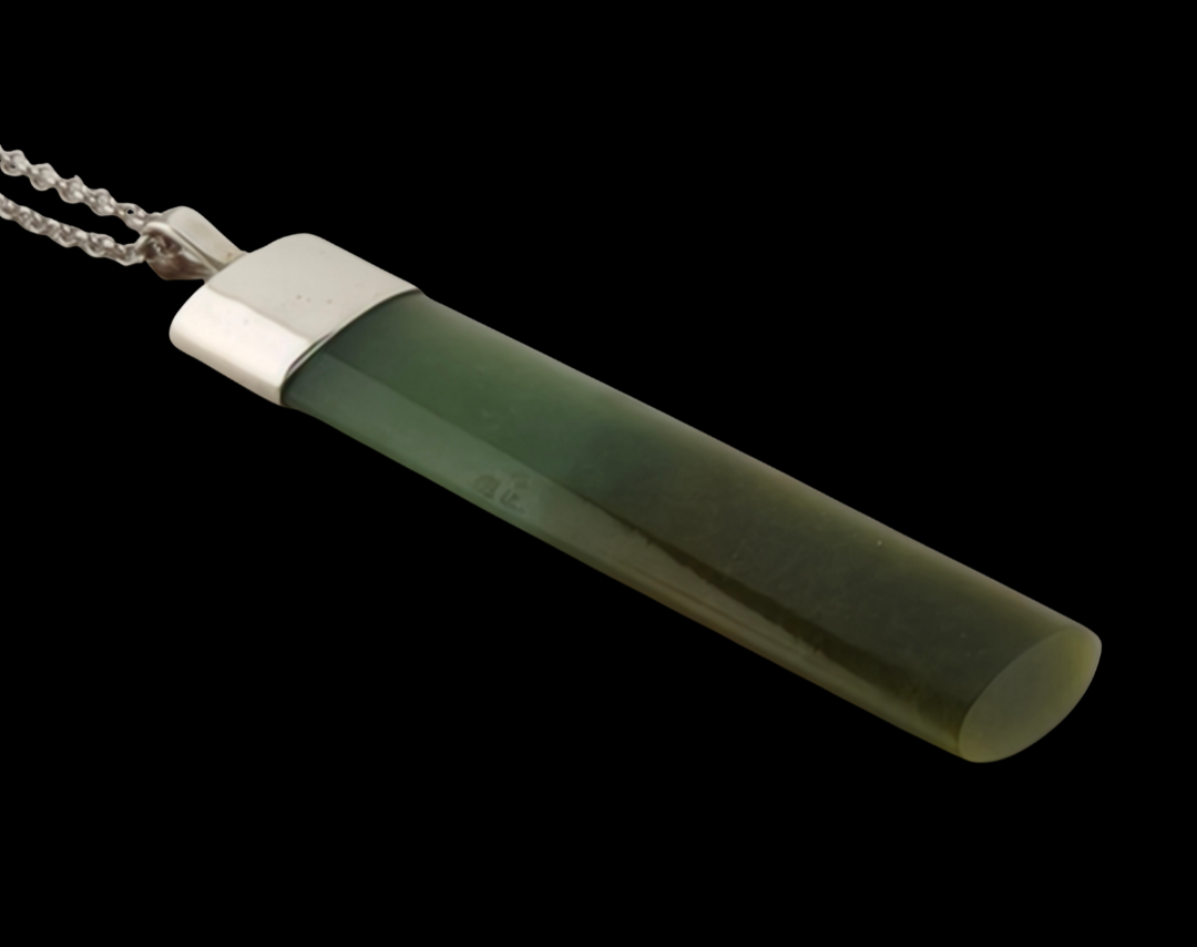 A greenstone cylindrical pendant necklace with a polished silver-toned cap and a silver ball chain, shown against a solid black background.