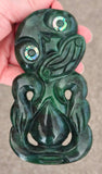 Green jade pendant with intricate carvings held in a hand against a neutral background