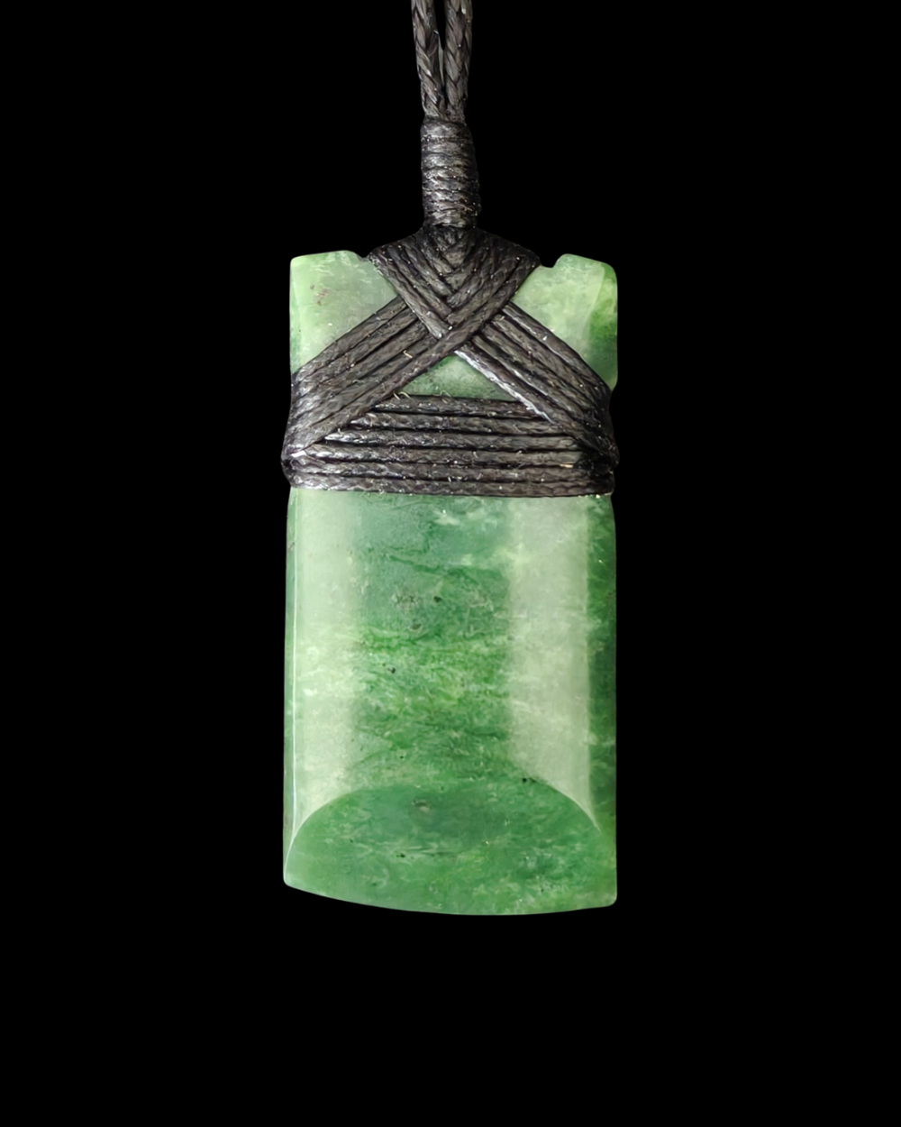Green jade pendant with woven cord on a black background Main image