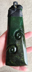 A dark green carved stone pendant with spiral motifs and a black cord wrap, held in a person's hand against a neutral background.