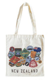An off-white canvas tote bag with long handles, featuring a collage of colorful New Zealand travel patches and the text 'NEW ZEALAND' printed in black at the bottom.