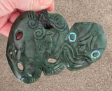 Green jade pendant with intricate carvings held by a hand on a neutral background