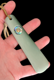 Light green ceramic tool with a decorative element held in a hand against a black background