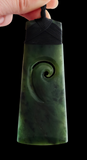 Green jade pendant with spiral design held by a hand against a black background