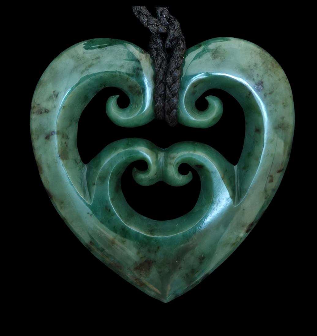 Greenstone heart-shaped pendant with intricate carvings on a black background