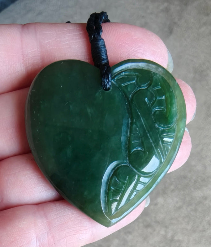 Heart-shaped green jade pendant held in a hand with a blurred background Main image