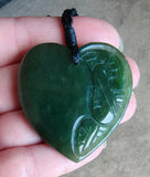 Heart-shaped green jade pendant held in a hand with a blurred background