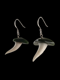 A pair of shark-tooth style drop earrings with dark green enamel crowns and ivory-colored teeth, suspended from silver fishhook wires, shown against a solid black background.