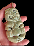 A carved stone pendant with a tribal face design, held in a hand against a solid black background.