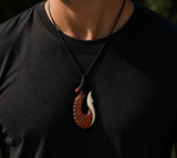 Person wearing a black shirt with a unique necklace featuring a bone pendant.