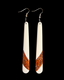A pair of long, tapered white dangle earrings with silver fishhook wires and a carved brown geometric pattern near the bottom, shown against a solid black background.
