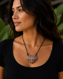 Woman wearing a black top with a necklace featuring a decorative pendant against a blurred green background