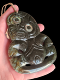 A hand holding a carved stone pendant with a loop at the top, shown against a solid black background.