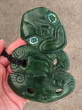 Green jade pendant with intricate carvings held by a hand on a beige background