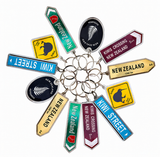 A set of New Zealand-themed road sign keychains arranged in a circular cluster on a white background. The keychains feature various stylized street signs including 'Kiwi Street', 'New Zealand', 'Kiwi Crossing 5min', and 'New Zealand 1200 m' in different colors with silver metal keyrings.