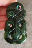 Greenstone pendant with intricate carvings held by a hand on a gray surface