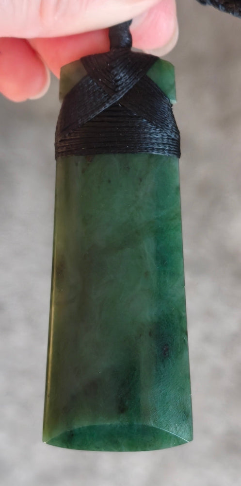 Green stone pendant with black cord held by a hand against a neutral background