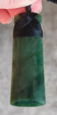 Green stone pendant with black cord held by a hand against a neutral background