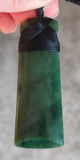 Green stone pendant with black cord held by a hand against a neutral background