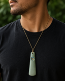 Man wearing a necklace with a green pendant against a blurred green background