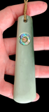Green stone pendant with a colorful center held in a hand against a black background