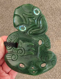 Green jade pendant with intricate carvings held by a hand on a neutral background