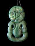 A carved green stone pendant paua inlay around the eyes, shown against a solid black background.
