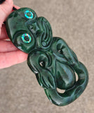 Green jade pendant with intricate carvings held by a hand on a neutral background